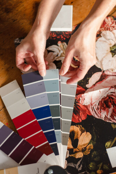 Paint chips and wallpaper are displayed on a beautiful wood table with a designer pointing to several options