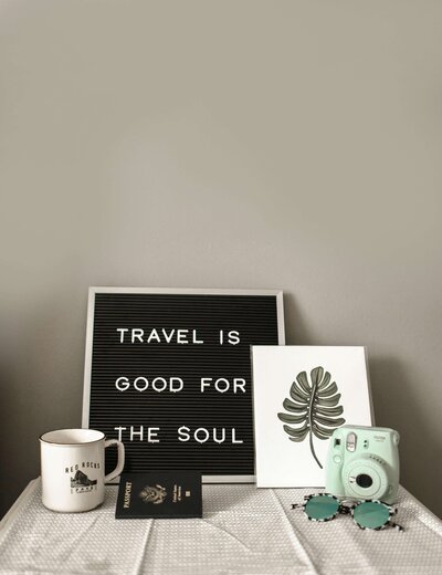 A tabletop with decor items including a sign reading 'Travel is good for the soul' alongside a small plant and mug, evoking a sense of adventure.
