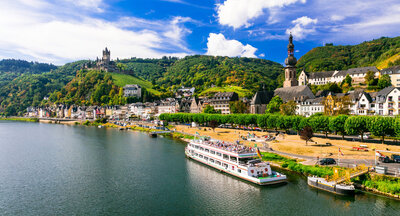 White river cruise ship sailing along the Moselle River past a charming European town with vineyards and castle views, symbolizing elegant small ship travel.

