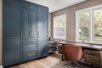 Contemporary office renovation featuring navy storage cabinets, rustic wood desk, and leather desk chair.