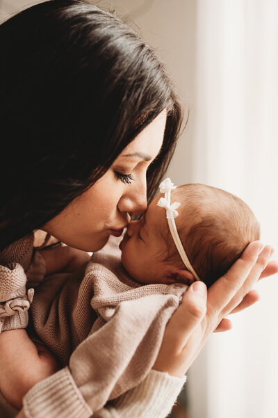 Basking in the motherhood glow, a new momma gives her newborn baby girl a little kiss on her nose during a newborn session at the studio of Nikii pix Photography in Bismarck. 