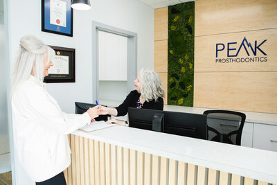 An image of Peak Prosthodontics staff warmly welcoming a patient highlights our dental consultation process—whether referred or booking directly, we’ll arrange a convenient appointment to discuss your dental needs, located in Lethbridge, Alberta.