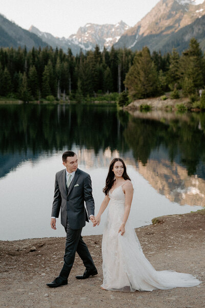 In the tranquility of Washington's natural landscape, a bride and groom take a leisurely stroll along the shores of a crystal-clear mountain lake. This photo, by a Washington wedding photographer, perfectly frames the couple against the majestic backdrop of towering mountains and evergreen forests. The couple's elegant attire contrasts with the rugged beauty of the surroundings, creating a stunning visual narrative of their wedding day adventure.