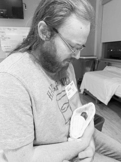 grieving dad holds stillborn baby in cradle at hospital