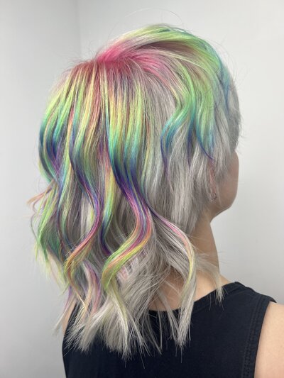 Image of client with hair that has been dyed a white blonde with a light, pastel, vivid, rainbow pattern.