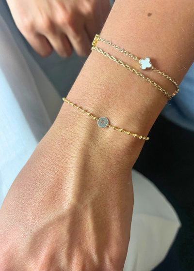 Close-up of layered permanent bracelets in gold and silver with a diamond charm on wrist.