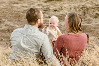 Parents sit in a field and hold their child. 