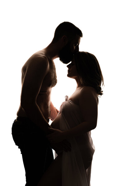 Expectant mother and father holding the baby bump with the father kissing the mother on her head