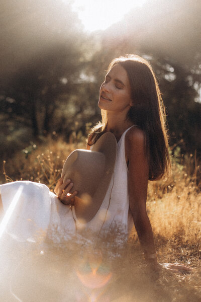 a young woman wearing a white dress and a hat sitting on a ground