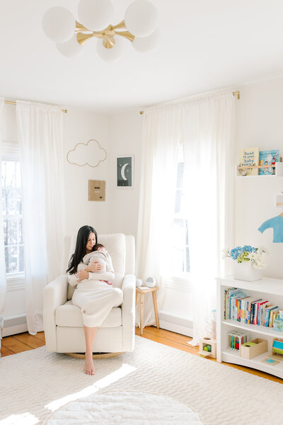 A woman sits in the nursery holding her newborn baby during her NJ portrait session