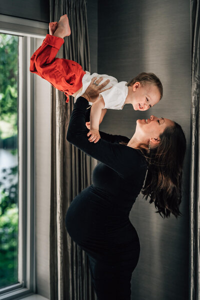 A pregnant mother holds her 2 year old son high up in the air during an in home lifestyle photo session in Minneapolis.