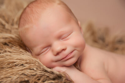A baby wearing a white sailor hat is lying down with eyes closed, resting their head on their hands. The baby holds a small American flag in one hand. Captured by a skillful Jacksonville maternity photographer, the serene scene highlights the innocence of new life against a dark blue backdrop.
