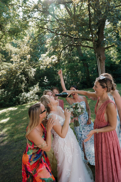 Bruid en haar vriendinnen dansen op het gras en drinken champagne.