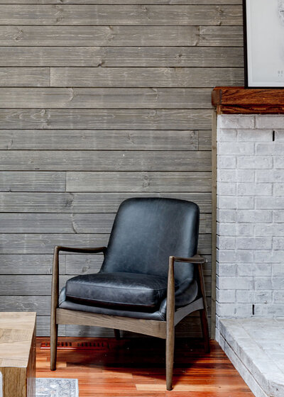 A nordic Interior Design by Winsome Home Interiors featuring a leather chair in front of a weathered wood wall. 