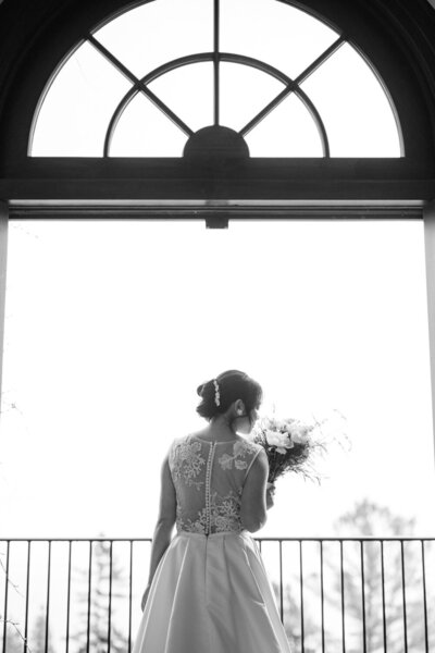 The bride gently inhales the scent of her bouquet by a sunlit window — a serene and refined moment captured during the preparations of an elegant wedding