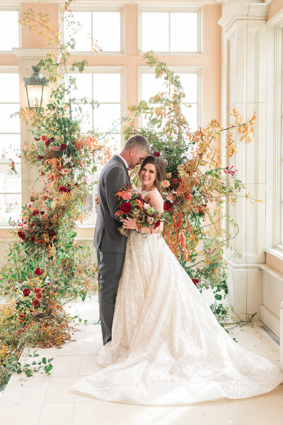 Bride and Groom pose in front of a floral backdrop