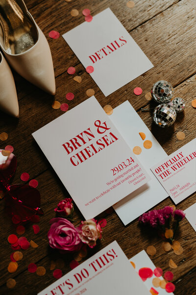 Flat lay of pink wedding stationery lay on the wooden floor of Elmore Court. 