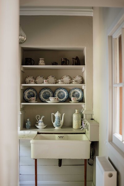 An old victorian pantry is photographed through a doorway. Light fills the space from outside.