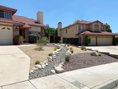 A front yard made mostly of gravel with a few water wise plants. There are large rocks creating a stream of small gravel running down the entire space. Landscaping Services done by Shamrock Solutions Construction based out of the Inland Empire California.