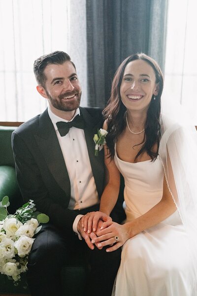 Newly wed couple sat, holding hands and smiling at the camera