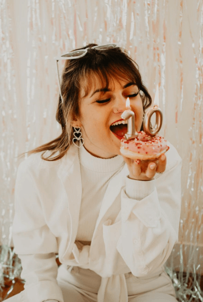 Laura, souriante s'apprête à mordre dans un donut décoré avec des bougies pour fêter ses 10 ans comme photographe professionnelle.