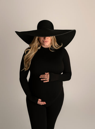 Maternity portrait in black bodysuit and oversized black hat at Austin photo studio