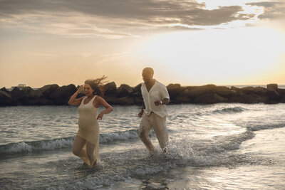 Engaged couple running along a New Jersey beach at sunset during a candid photoshoot