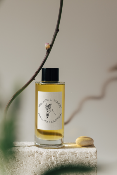 A clear glass bottle with a black cap labeled “Phillipa Leseberg” stands on a textured surface next to a smooth yellow stone, evoking the thoughtful brand strategy behind Sweet Pea Ink Creative. A thin branch rests in the background.