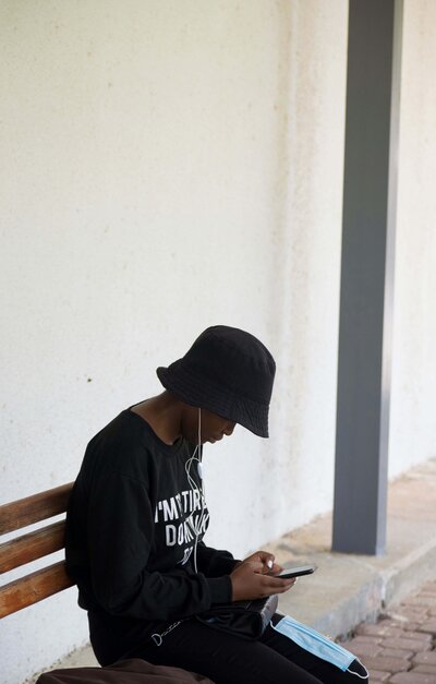Black teen in hat on phone outside on bench