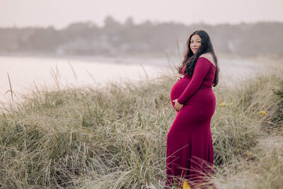 Pregnant woman in deep red dress in tall grass at beach