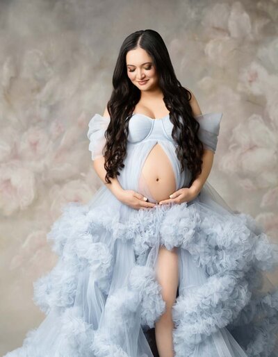 Maternity portrait of brunette woman with long curls wearing a light blue tulle gown