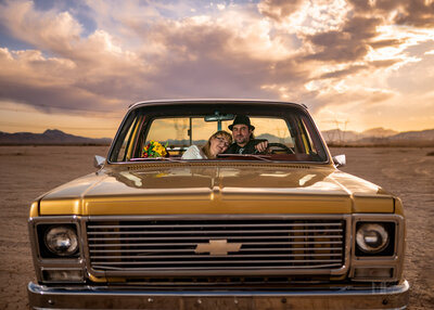 dry lake bed elopement classic gold chevy truck hat on groom holding bride sunset golden hour by las vegas wedding photographers mk delacy