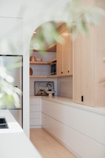 Minimalist kitchen featuring light wood cabinets and white drawers, with open shelves displaying decorative items. Experience bespoke interior design in Newcastle NSW that transforms your space into a stylish sanctuary.