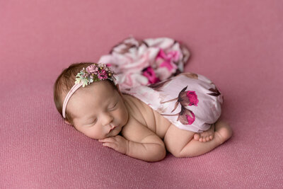 newborn baby girl sleeps on her belly on a pink background, wrappined in floral fabric