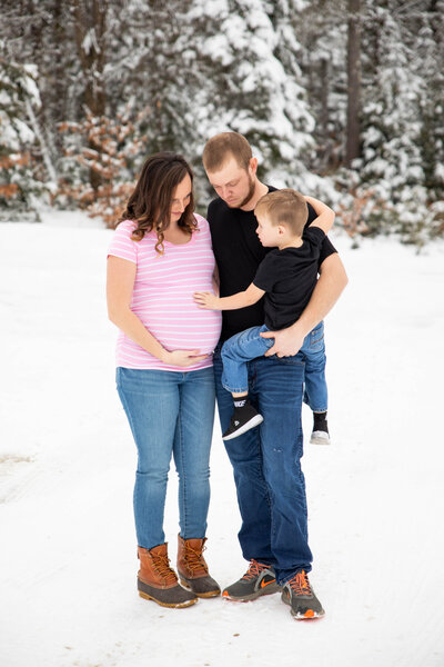 Family being photographed in snow, Mom is expecting | Taken by Maine Maternity Photographer