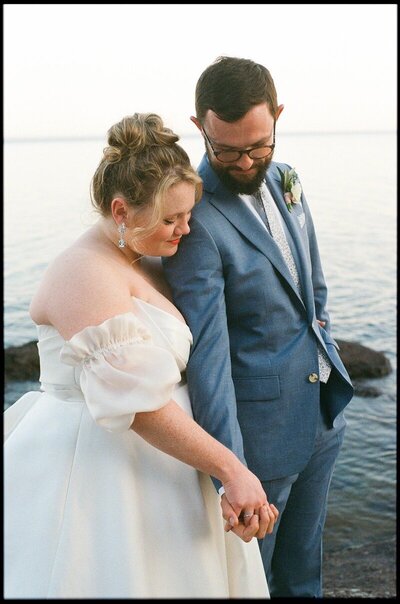 bride and groom hold hands near the water dressed for their wedding photographed by minnesota photographer tom thornton