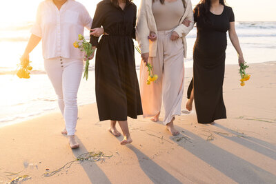 Women linking arms holding flowers on the beach at sunset