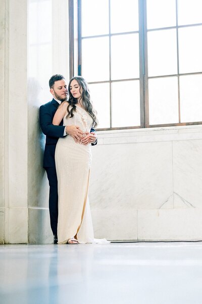 Couple standing in front of a large window  leaning against marble walls in a museum in Atlanta GA Photographer Rocheal Matthews Wedding Planning Tinted Events Design and Planning
