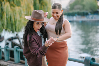 Lesbian couple admiring engagement ring after a surprise proposal near the Eiffel Tower at Bir-Hakeim Bridge — captured by Paris proposal photographer Rachael Laporte.