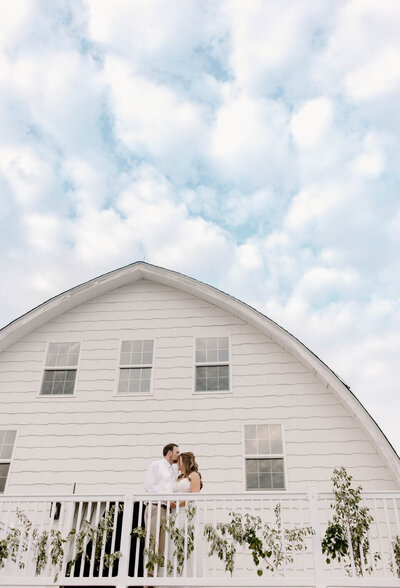 bride and groom kiss on balcony at white barn wedding venue at vanderwende acres seaford delaware