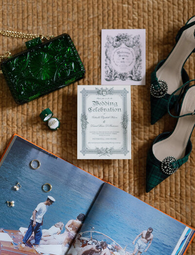Wedding invitation flat lay with shoes, purse and rings on a book.