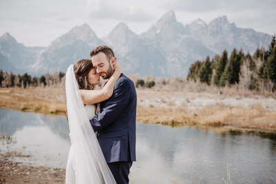wyoming elopement with bride and groom embracing on another with the grand tetons in the distance as they embrace slowly and romantically in front of a river captured by jackson hole photographers