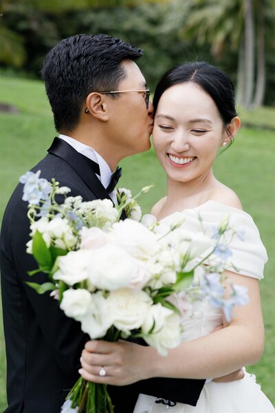 A person kissing their partner's head as they hold a bouquet of flowers on their wedding day 