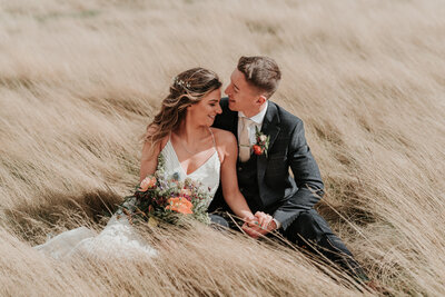 Bride & Groom sitting next to each other in a long grass field at Two Woods Estate, Pulborough