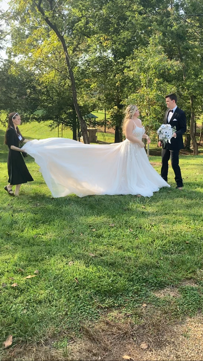 Tennessee Wedding Photographer, Jennifer Cooke fluffing a bride's dress under bright, summer trees