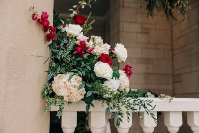 Red and white flowers with greenery sitting on stone railing