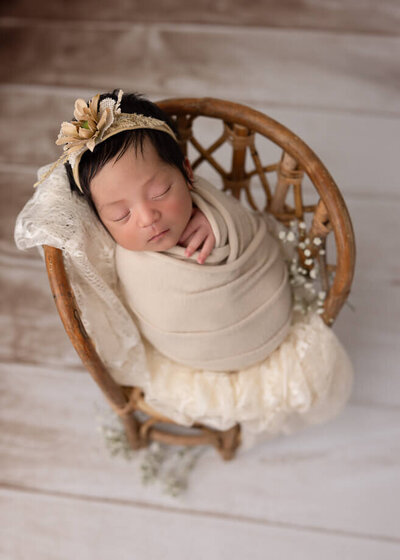 baby in a beige swaddle on a lace draped bench with babies breath florals as an accent
