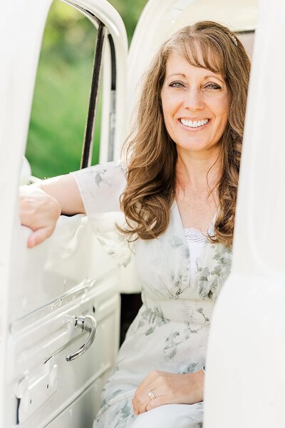 Jennifer Hall smiling and sitting in a white vintage truck outdoors.