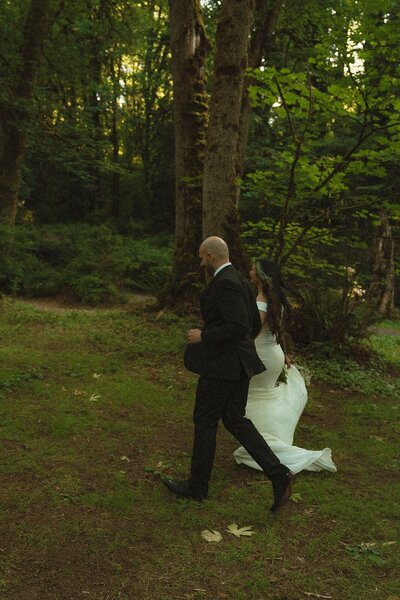 Bride and groom walking together through a forest clearing during their elopement