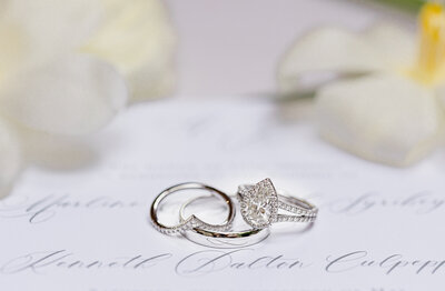 set of wedding rings and groom band set on top of wedding invitations